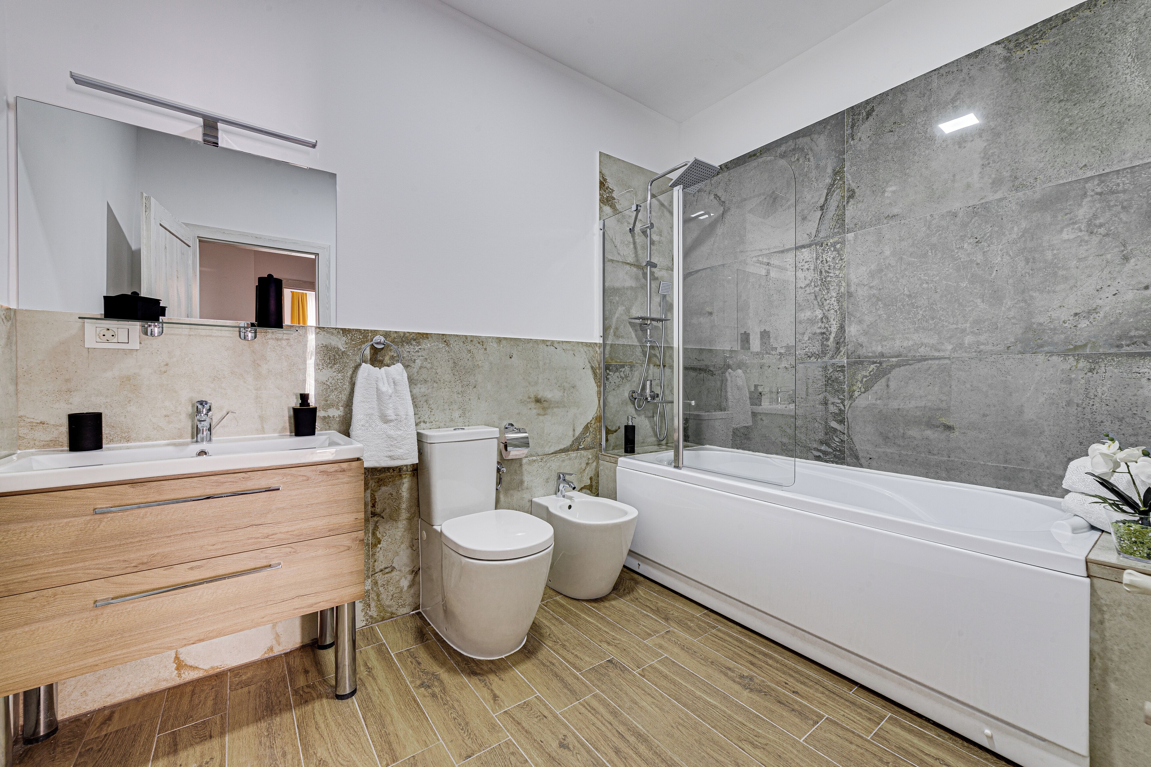 A modern bathroom with a large mirror, two sinks, a toilet, a bidet, and a bathtub.