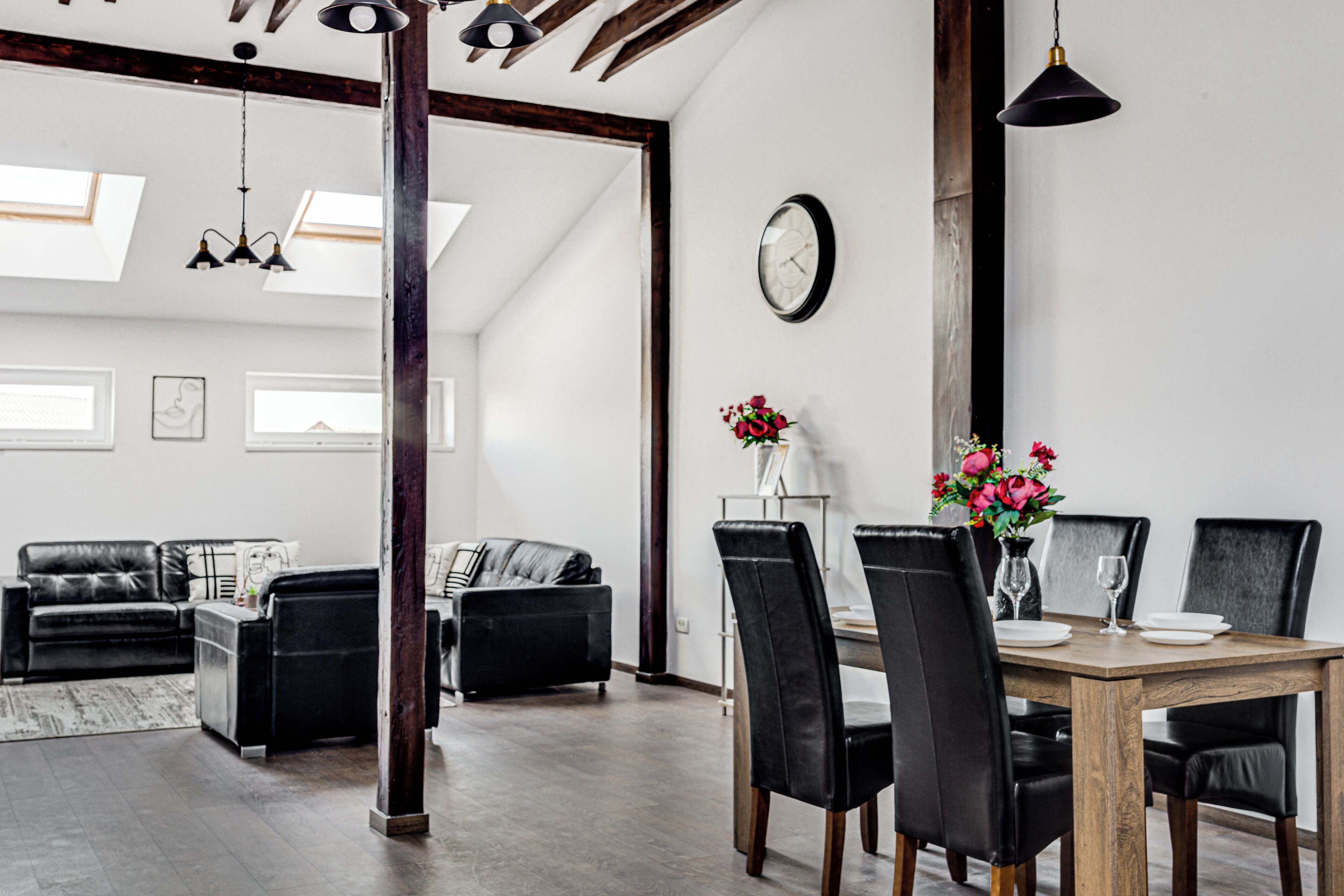 Una sala de estar moderna con comedor, que incluye una mesa de comedor de madera, sillas negras y un jarrón con flores.