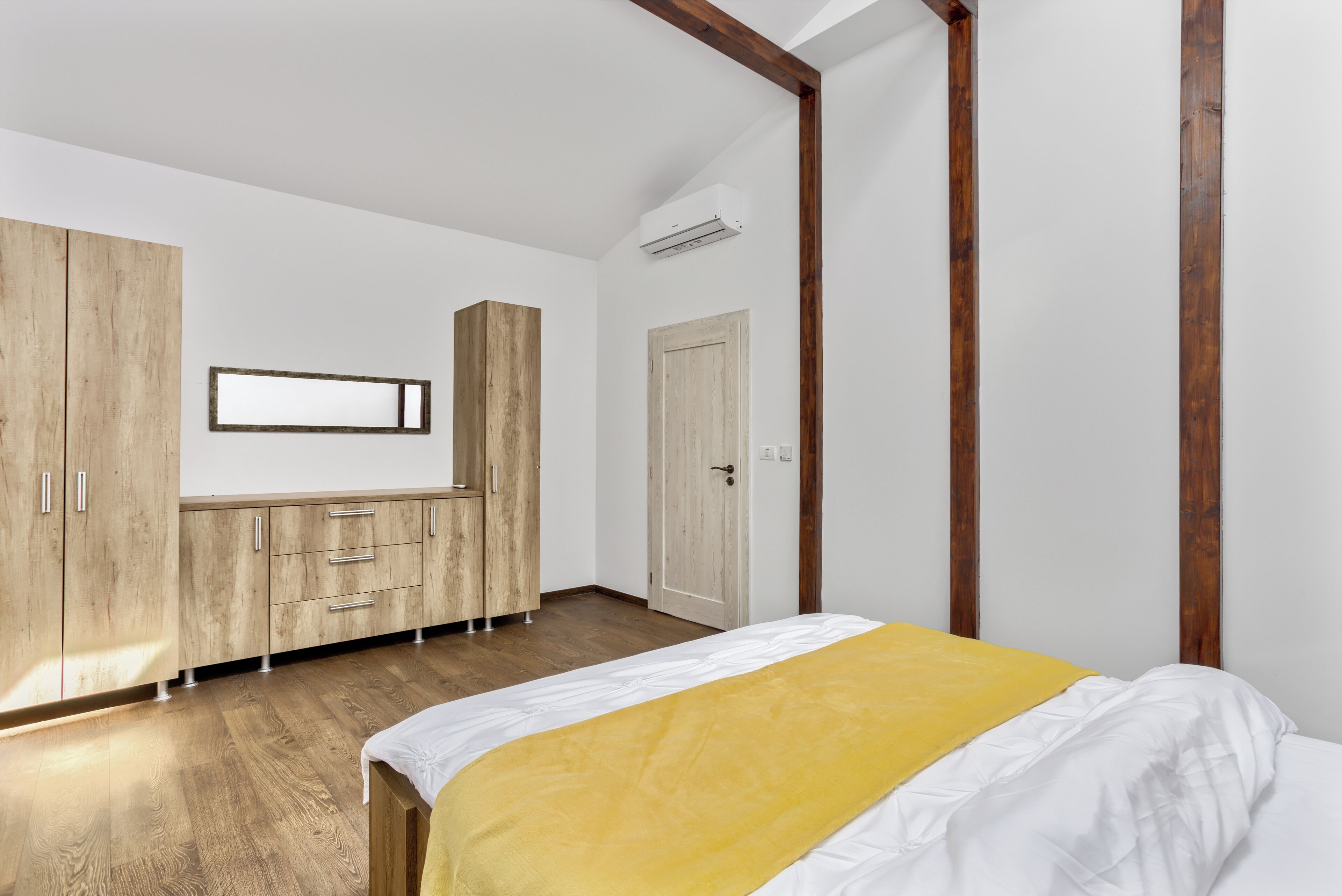 Een slaapkamer met een bed, een houten garderobe en een spiegel aan de muur.