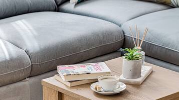 A cozy living area with a grey sofa, a wooden coffee table, a white coffee cup, a book, and a small potted plant with reed sticks.