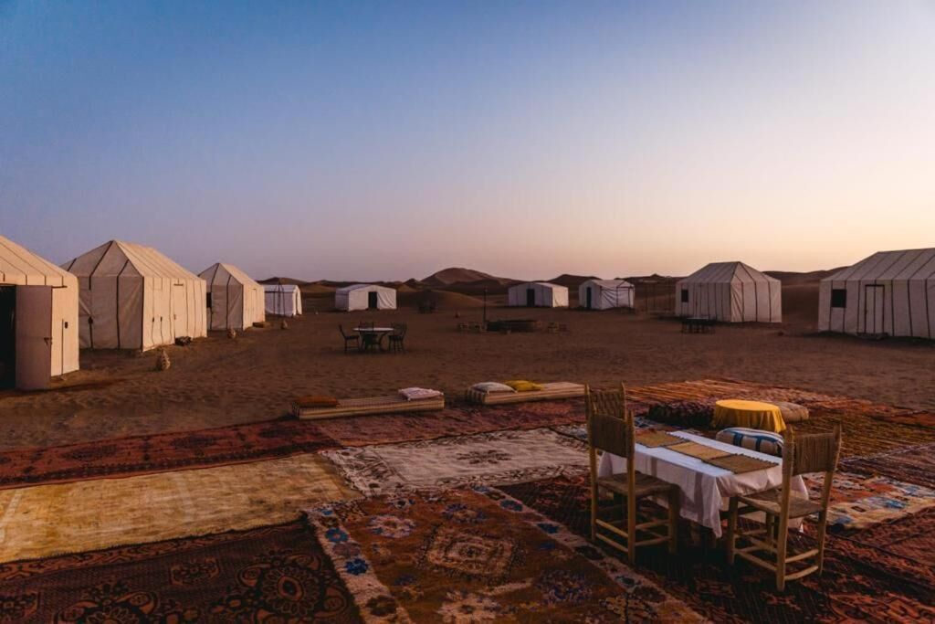 A series of white tents arranged in rows on a flat landscape, with a table and chairs set up in the foreground.
