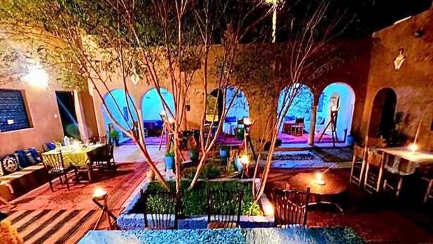 An outdoor dining area with tables and chairs, a decorative fountain, and a view of the interior through an archway. - Riad Assia (Foum Zguid)