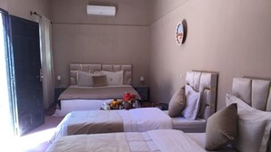 A hotel room with two beds, a bedside table with a lamp, a wall-mounted air conditioner, and a small decorative item on the wall. - Riad Assia (Foum Zguid)