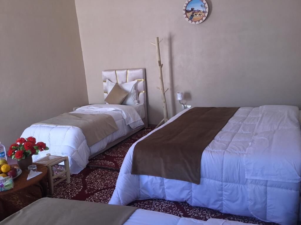 A hotel room with two beds, a small table with a vase of flowers, and a wall-mounted clock.