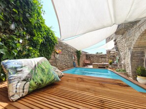 Et poolområde med træterrasse, stenvægge og et hvidt markise.