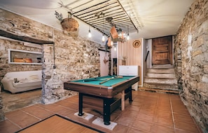 Une table de billard dans une pièce aux murs en pierre, avec un canapé et un escalier.