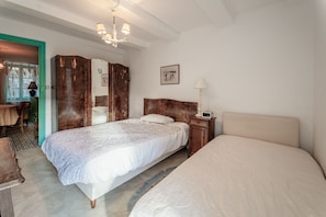Un dormitorio con dos camas, un armario de madera, una mesita de noche con lámpara y un cuadro enmarcado en la pared.