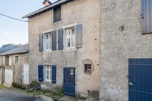 A two-story building with a stone facade, multiple windows with shutters, and a visible door.