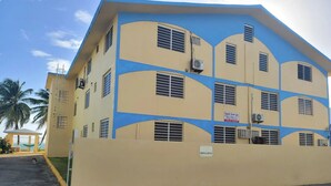 Un edificio de varios pisos con fachada amarilla y detalles azules, con varias ventanas y unidades de aire acondicionado.