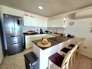 Una cocina con refrigerador, microondas, pileta y un reloj en la pared.