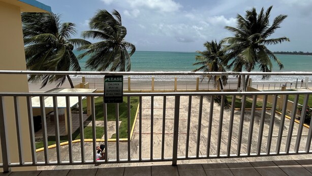 Un balcón con vista a la playa, palmeras y un letrero que indica que los niños deben ser supervisados en todo momento.