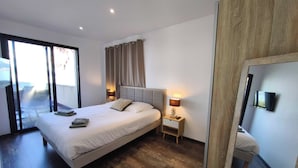 A modern bedroom with a large bed, two bedside tables with lamps, a sliding glass door leading to a balcony, and a wooden floor. - A serene stay with a sea view (Grosseto-Prugna)