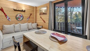 A wooden interior with a sofa, dining table, and large windows.