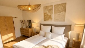A bedroom with a bed, bedside lamps, a wooden wardrobe, and abstract wall art. - Pier 2: 200m to the sea, terrace, sauna, fireplace (first floor) (Scharbeutz)