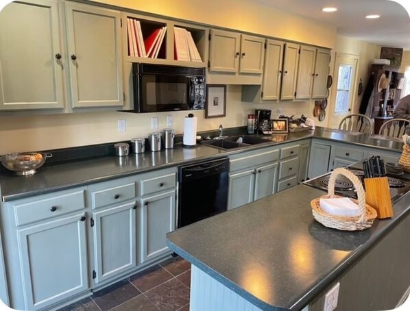 A kitchen with light grey cabinets, a black microwave, and a dishwasher. There is a sink and a countertop with various items.