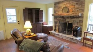 A living room with a stone fireplace, leather furniture, and a bookshelf.