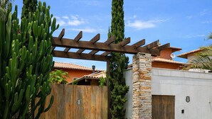 Un edificio con un pilar de piedra, una pérgola de madera y una planta de cactus.
