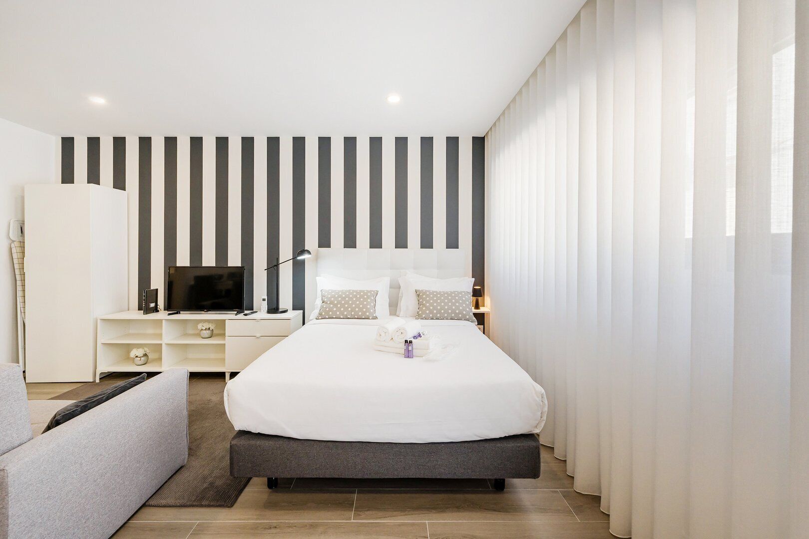 A modern bedroom with a large bed, a TV, a bedside table, and a wardrobe.