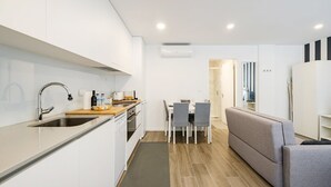 A modern kitchen with white cabinetry, a stainless steel sink, and a dining area with a grey sofa and chairs.