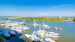 Un puerto deportivo con numerosas embarcaciones amarradas, un puente al fondo y un cielo azul despejado.