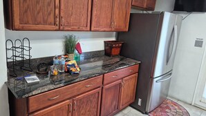 A kitchen with wooden cabinets, a granite countertop, a stainless steel refrigerator, and a small rug.