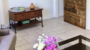 A room with a wooden sliding door, a small table with a vase, a wall-mounted shelf with decorative items, and a painting of hot air balloons.