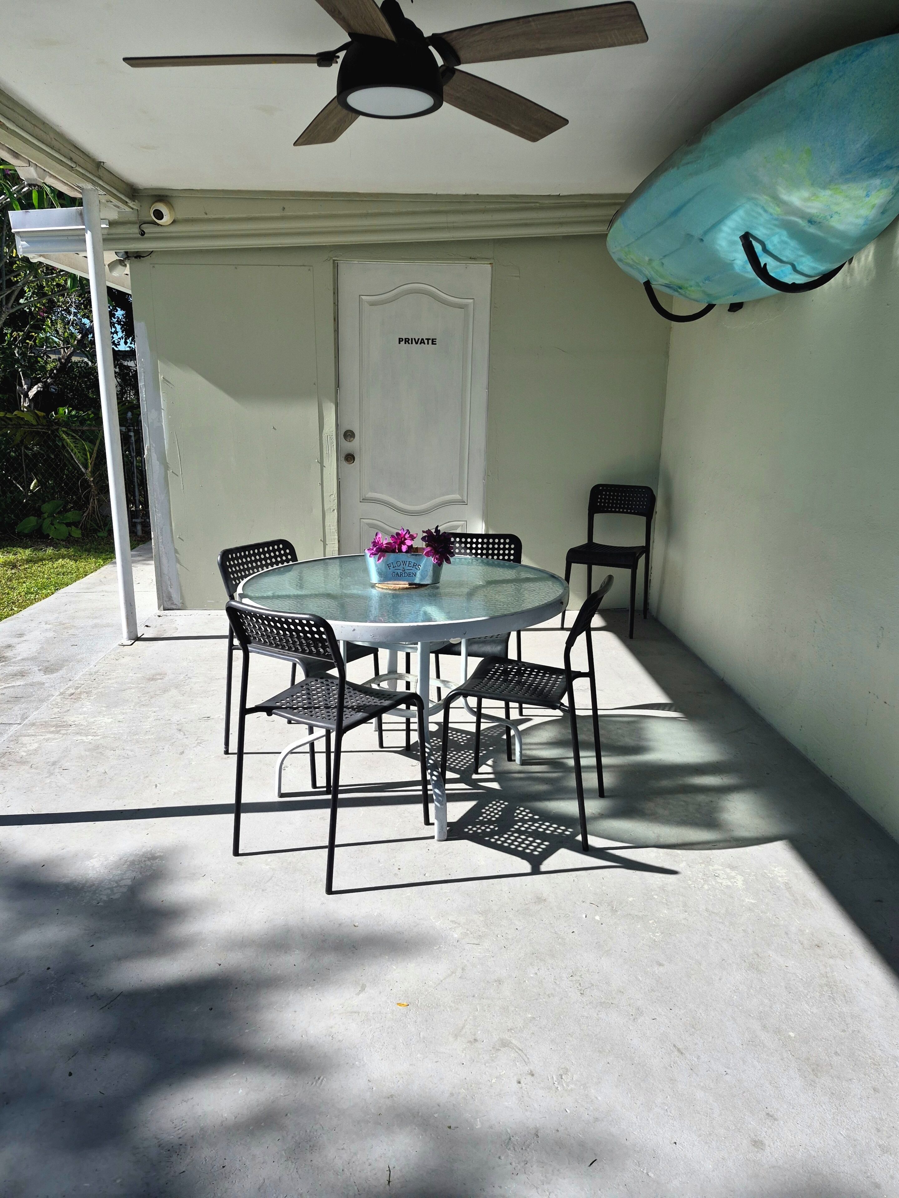 A covered patio with a table and chairs, a ceiling fan, and a door labeled 'PRIVATE.'