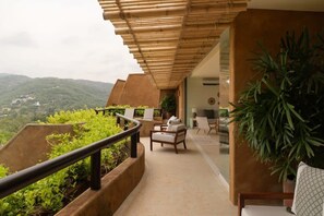 Een balkon met uitzicht op een bergachtig landschap, voorzien van een bank en stoelen, en een grote potplant.