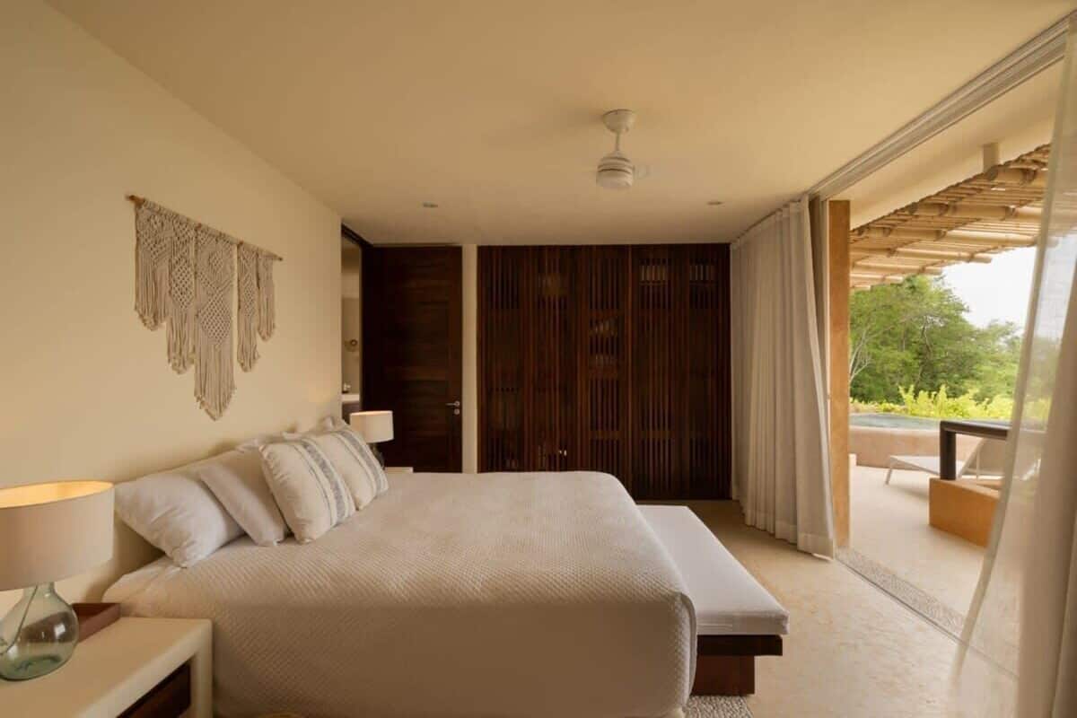 Ein Schlafzimmer mit einem großen Bett, einem Nachttisch, einem Deckenventilator und Blick ins Freie.