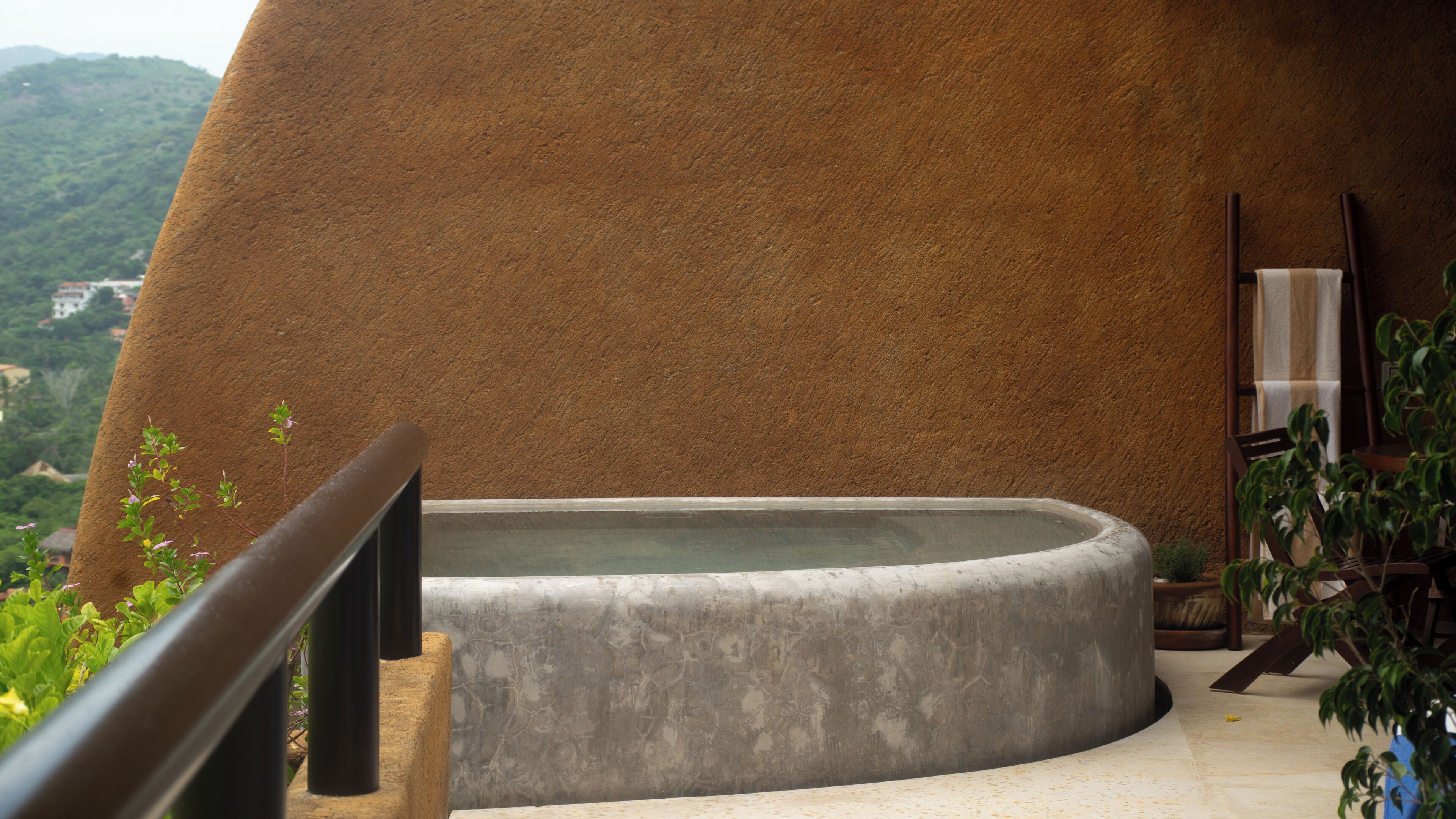Un bain à remous avec un mur en pierre en arrière-plan, une chaise en bois et une rambarde.