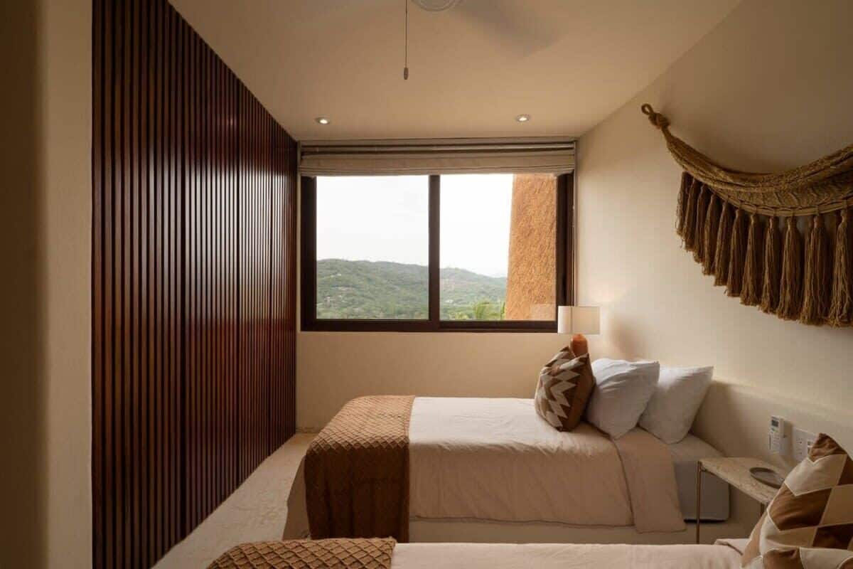 Ein Schlafzimmer mit großem Fenster, einem Bett mit brauner Decke und einer Wandlampe.