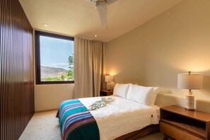 Een hotelkamer met een groot bed, een nachtkastje met lamp, een raam met gordijnen en uitzicht op de omgeving.