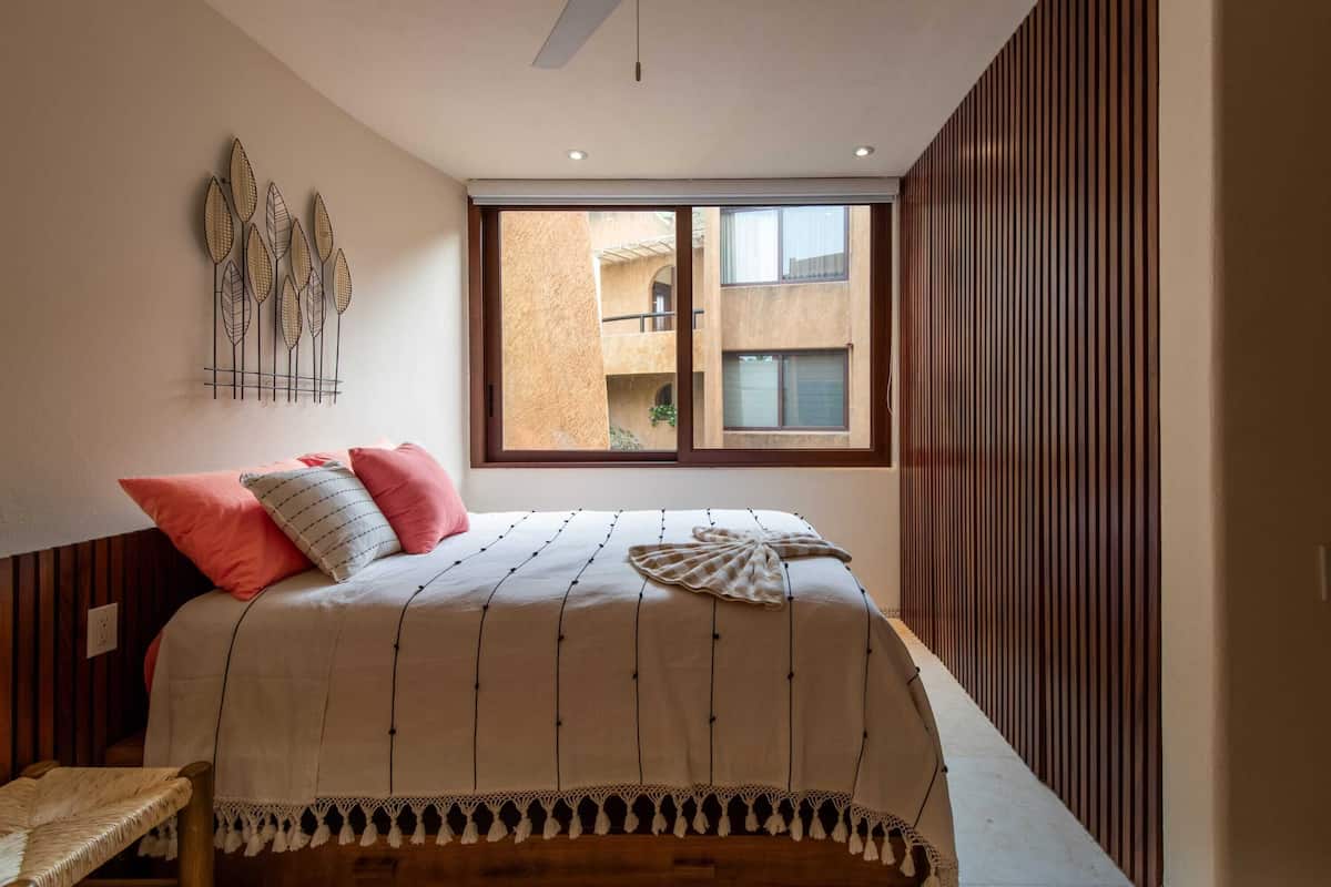 Ein Schlafzimmer mit einem großen Fenster, einem Bett mit gestreifter Bettdecke und einem an der Wand befestigten Dekorationsgegenstand.