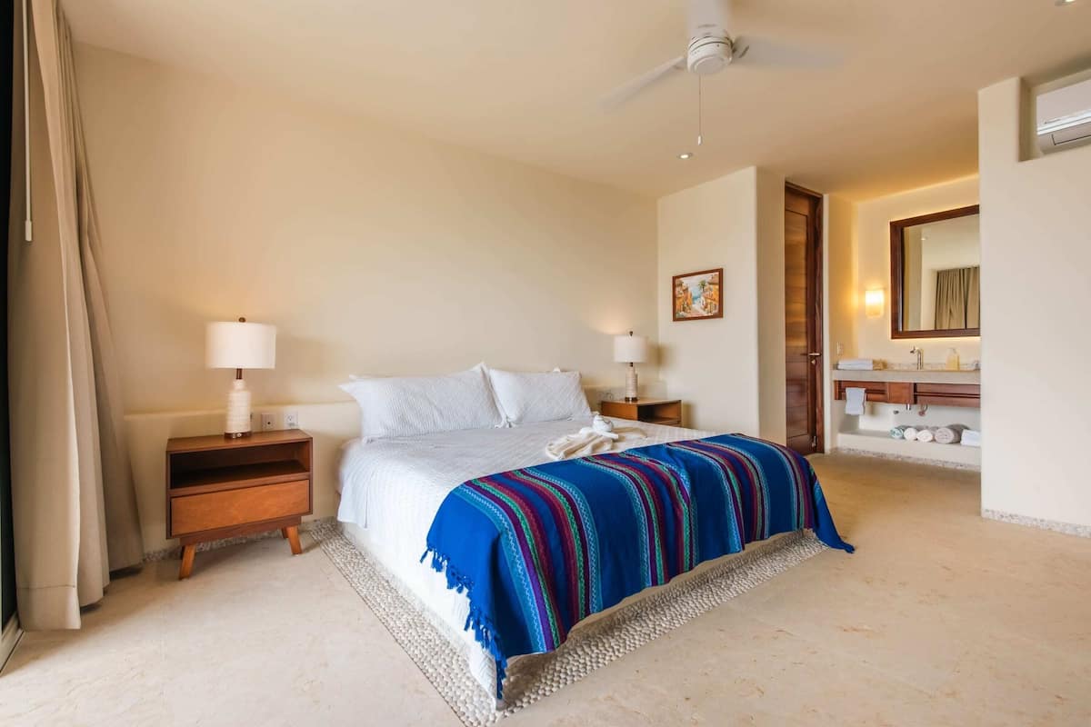 Ein Hotelzimmer mit Bett, Nachttischen, einem Spiegel und einem durchgegangenen Tür angedeuteten Badezimmer.