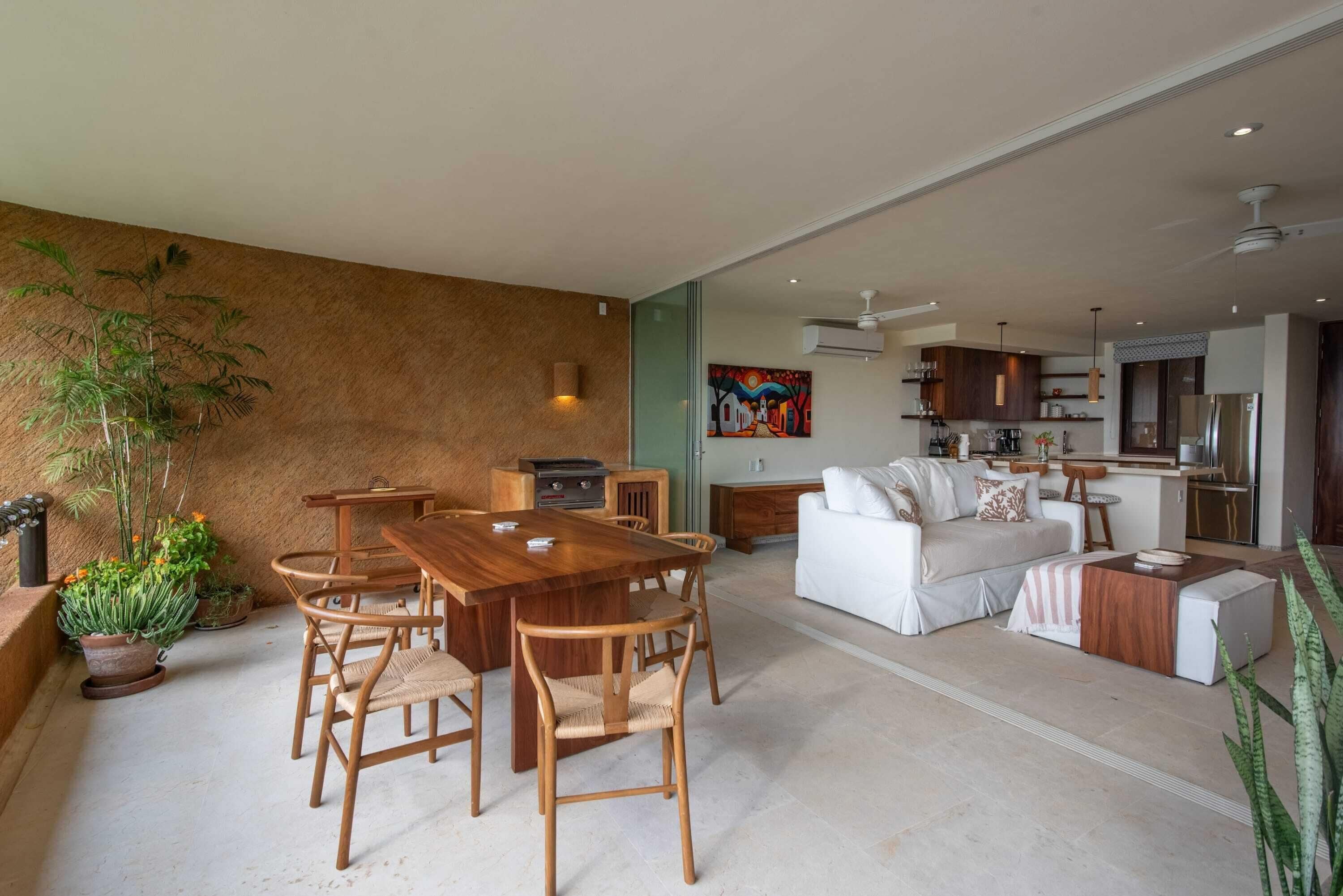 A spacious living area with a wooden dining table, white sofa, and a kitchen in the background.