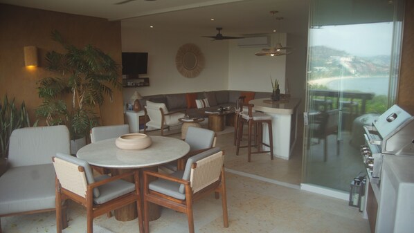 A dining area with a round table, chairs, a television, and a view of the outdoors.
