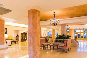 Un vestíbulo amplio con columnas de mármol, asientos cómodos y un candelabro.