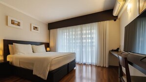 Una habitación de hotel con cama, escritorio y un amplio ventanal con cortinas.