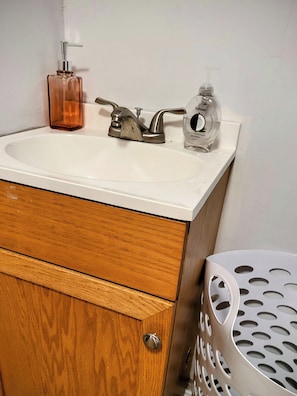 A bathroom with a white sink, two soap dispensers, a wooden cabinet, and a metal laundry basket. - Fiddlers Lake Cabin, Galax Va, Fishing, New River Trail, Fancy Gap, Mountains  (Galax)