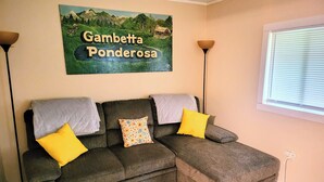 A room with a sectional sofa, a painting of a landscape, a window with blinds, and a lamp. - Fiddlers Lake Cabin, Galax Va, Fishing, New River Trail, Fancy Gap, Mountains  (Galax)