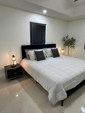 Une chambre à coucher comprenant un lit, une table de chevet, une lampe, une fenêtre avec des stores et une plante fixée au mur.
