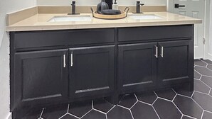A bathroom with two sinks, black cabinets, and a hexagonal tile floor.