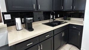 A modern kitchen with dark cabinets, a white countertop, and a coffee maker.