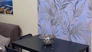 Ein Essbereich mit einem schwarzen Tisch und vier schwarzen Stühlen, einer dekorativen Schale auf dem Tisch und floraler Tapete im Hintergrund.