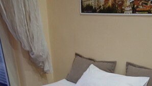 Ein ordentlich bezogenes Bett mit roter Bettdecke und weißen Kissen, ein gefaltetes weißes Handtuch auf dem Bett und ein gerahmtes Bild an der Wand.