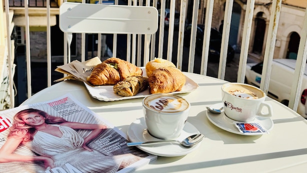 A table with pastries, a cup of coffee, and a magazine on a balcony overlooking a cityscape with historic buildings. - Guest House San Giacomo*Holidays in Apulia* in the centre to 5 min Teatro Curci (Barletta)