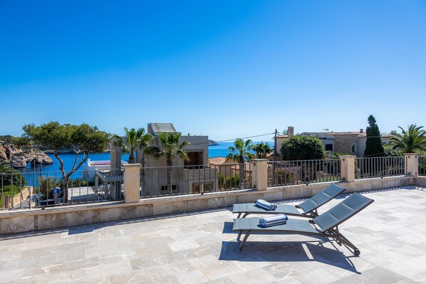 A rooftop terrace with lounge chairs, a stone floor, and a view of the sea.
