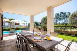 Un área de comedor al aire libre con piscina, muros de piedra y follaje.