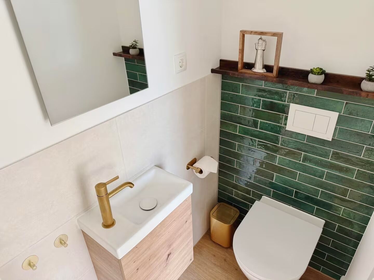 Un baño con lavamanos blanco, grifo dorado, salpicadero de azulejos verdes y retrete blanco.