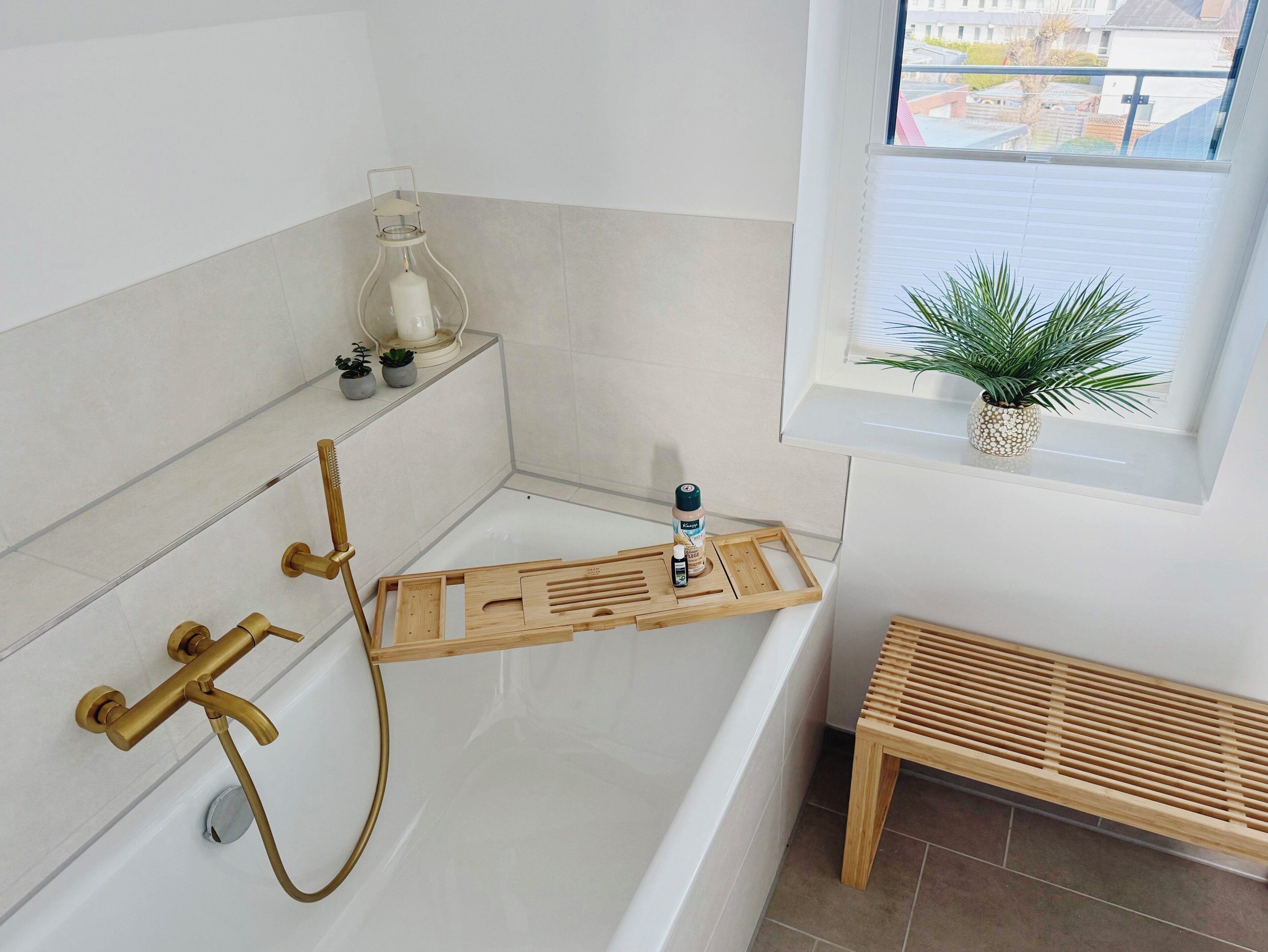A bathroom with a bathtub, a wooden shelf with toiletries, a window with a plant, and a wooden bench.